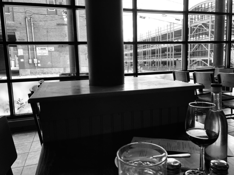 The black and white image of a tables inside a restaurant with a partial view of a wine glass and glass of water